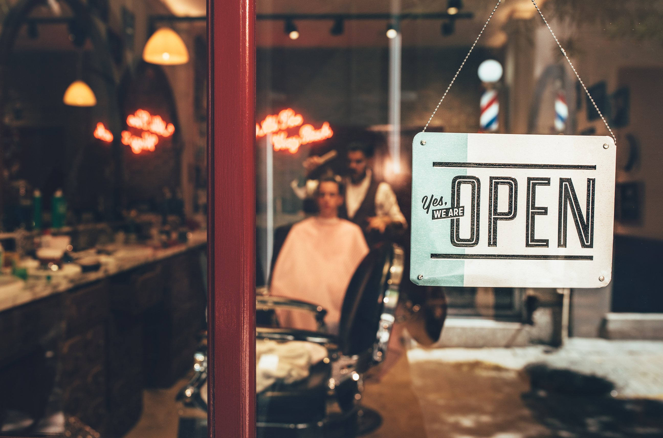 Barber shop window with open sign and barber working indoors